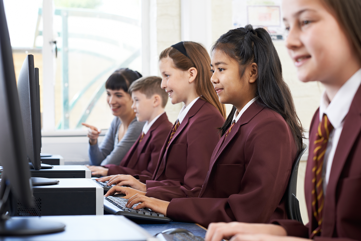 Education IT support supporting a group of school students work at desktop computers